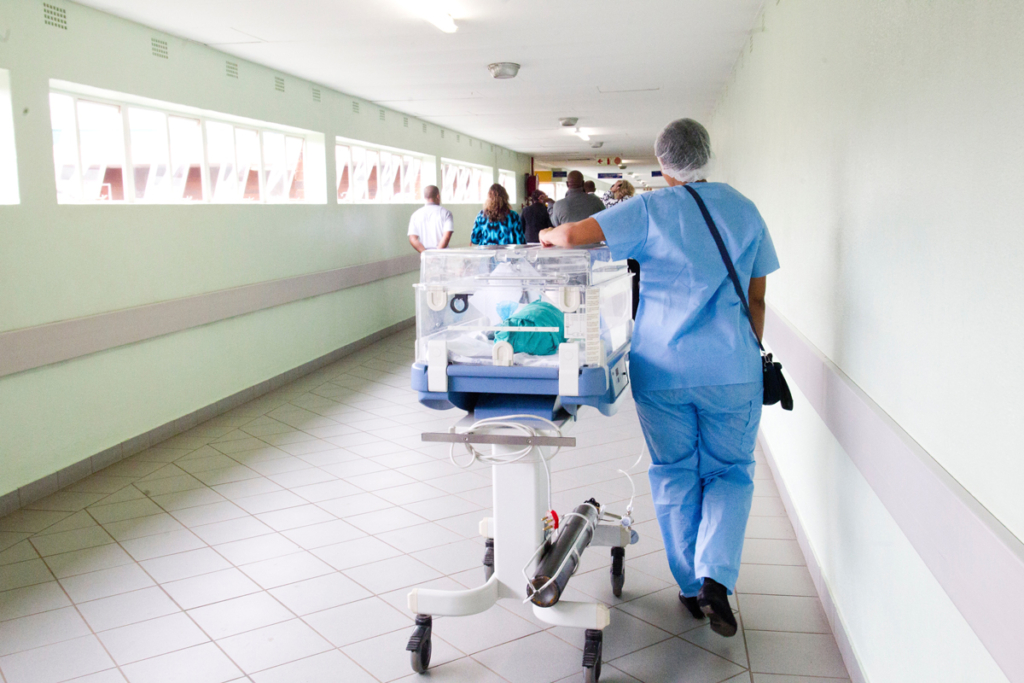 A medical professional pushes an incubator along a hospital corridor. Photo by Hush Naidoo on Unsplash